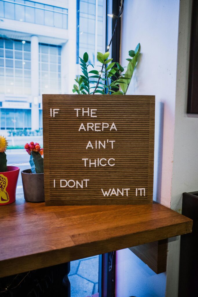 Wooden letter board with humorous message about arepas in a cozy café setting by the window.